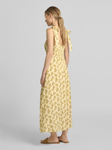 Frauenmodel trägt Midikleid mit floralem Allover-Print Modell 'Yaselin' von YAS aus Reine Baumwolle, Taillierte Passform, Ärmelloses-Design, Rückenlänge bei Größe 36: 128 cm, Brustweite bei Größe 36: 33 cm, gelbes Muster, weich fallender Stoff, Ganzkörperansicht Rückansicht.