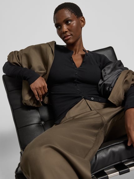 Frauenmodel trägt Langarmshirt mit durchgehender Knopfleiste von black palms in Schwarz, unifarbene Optik, Rundhalsausschnitt, Nahaufnahme Oberkörper.