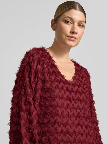 Frauenmodel trägt Minikleid mit strukturierter Oberfläche von Selected in unifarbenem Dunkelrot mit V-Ausschnitt, Nahaufnahme Oberkörper.
