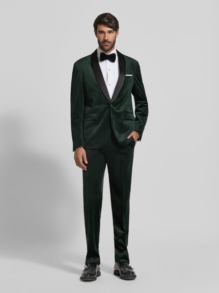 Männermodel trägt Slim Fit Anzug aus Samt von Lindbergh in Dunkelgrün mit Schalkragen, Knopfverschluss und Pattentaschen, Ganzkörperansicht von vorne.