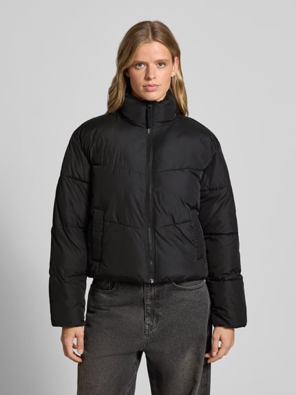 Frauenmodel trägt Steppjacke mit Stehkragen und Eingrifftaschen von JJXX, schwarz, Regular Fit, glatte Struktur, Ganzkörperansicht von vorne. Rückenlänge 58 cm, Schulterbreite 52 cm, Brustweite 58 cm, Ärmellänge 60 cm.