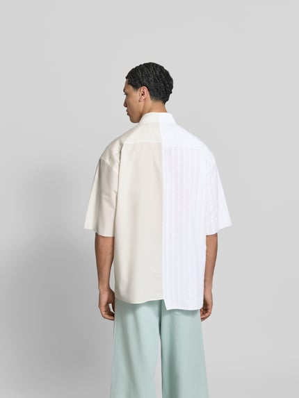 Męski model nosi Regular Fit Freizeithemd aus Baumwolle od MM6 Maison Margiela, jasny beż i biel, krój regular fit, półrękaw, tkanina bawełniana o asymetrycznym wzorze, długość tyłu w rozmiarze 50: 79 cm, szerokość ramion w rozmiarze 50: 48 cm, długość rękawa w rozmiarze 50: 30 cm, widok całej sylwetki z tyłu.