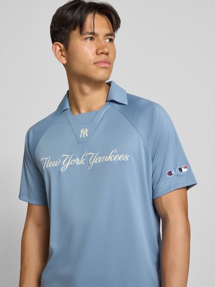 Männermodel trägt Relaxed Fit Poloshirt mit Logo-Stitching von Champion in Hellblau, glatte Textur, Kurzarm, Nahaufnahme Oberkörper.