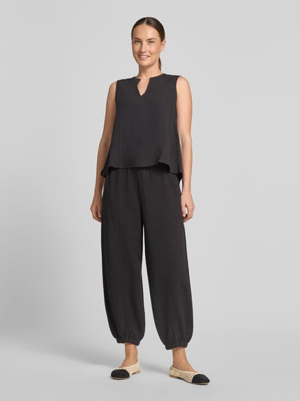 Frauenmodel trägt Relaxed Fit Hose aus Viskose-Mix Modell 'Myha' von OPUS in Schwarz mit elastischem Bund, Tunnelzug, Eingrifftaschen, verkürzter Passform und elastischen Beinabschlüssen, Ganzkörperansicht von vorne.