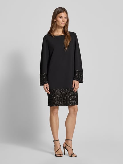 Vrouwenmodel draagt Relaxed Fit Mini-jurk met pailletten van s.Oliver BLACK LABEL, effen look, minilengte, boothals, lange mouw, zonder sluiting. Ganzkörperansicht von voren.