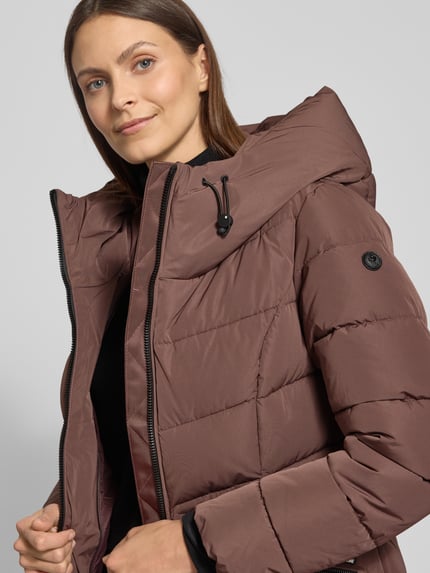 Modelka kobieca nosi Steppjacke mit Kapuze od khujo, kolor brązowy, regular fit, stójka, zamek, detal z logo, zbliżenie na górną część ciała.