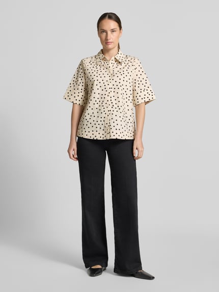 Frauenmodel trägt Hemdbluse aus reiner Baumwolle Modell 'MALAY' von FREE/QUENT, beige mit dunklen Punkten, kurzärmelig, Ganzkörperansicht von vorne.