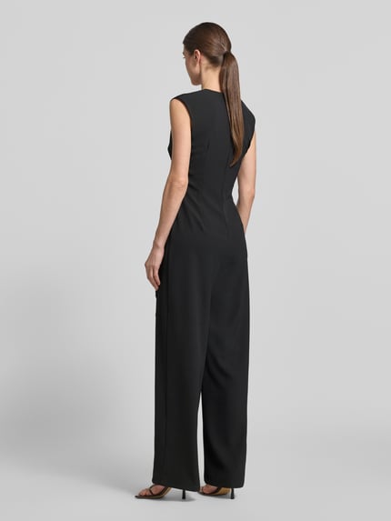 Männermodel trägt Regular Fit Jumpsuit mit Zierbesatz von Rinascimento, czarny, materiał elastyczny, satyna, krój regular fit, długość całkowita 148 cm, szerokość w rozmiarze S 44 cm, długość wewnętrzna nogawki 82 cm, talia dopasowana, optyka zakładek, widok całej sylwetki z tyłu.