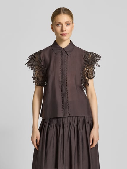 Vrouwenmodel draagt Regular Fit Blouse met kanten details model 'MOLLY' van Copenhagen Muse, stretch-materiaal, hemblousekraag, verborgen knoopsluiting, ruglengte 62 cm, mouwlengte 10 cm, donkere tint, bloemvormige kantstructuren, gladde stof, vooraanzicht bovenlichaam.