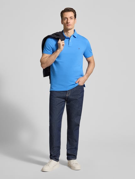Männermodel trägt Regular Fit Poloshirt aus bawełny-mix von Tommy Hilfiger, efekt: jednolity kolor, wyhaftowane logo, kołnierzyk polo, zapięcie na 2 guziki, krótki rękaw, wykończenie z rozcięciem, pika; Ganzkörperansicht von vorne