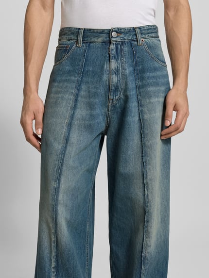 Mężczyznamodel nosi Wide Fit Jeans im 5-Pocket-Design von MM6 Maison Margiela z bawełny, ozdobne szwy, zapięcie na guzik i zamek błyskawiczny, stylizowane na denim, jasnoniebieskie odcienie, wyraźna faktura materiału, przód spodni, detal, zbliżenie na górną część nogawek, Nahaufnahme Oberkörper.