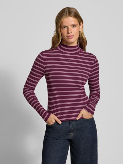 Frauenmodel trägt Slim Fit Langarmshirt aus Baumwoll-Mix von Tommy Jeans, lila mit weißen Streifen, glatte Textur, Ganzkörperansicht von vorne, Damen Langarmshirt von Tommy Jeans.