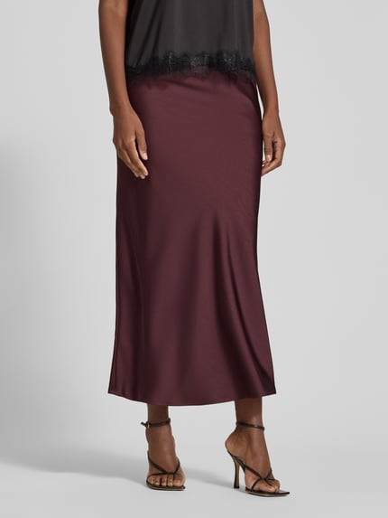 Frauenmodel trägt Maxirock aus Satin Modell 'Vicky' von Neo Noir in dunklem Rotbraun, glatte Textur, körpernahe Passform, Nahaufnahme Unterkörper. Elastischer Bund, Material-Mix und Länge laut Produktbeschreibung.