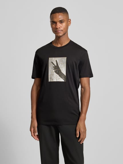 Männermodel trägt T-Shirt mit Motiv-Print von ARMANI EXCHANGE, Reine Baumwolle, Regular-Fit, gerippter Rundhalsausschnitt, Ganzkörperansicht von vorne.
