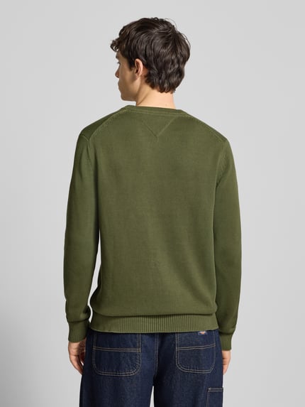 Männermodel trägt Regular Fit Strickpullover aus reiner Baumwolle von Tommy Jeans in Olivgrün, unifarben, Rundhals, Ganzkörperansicht Rückansicht.