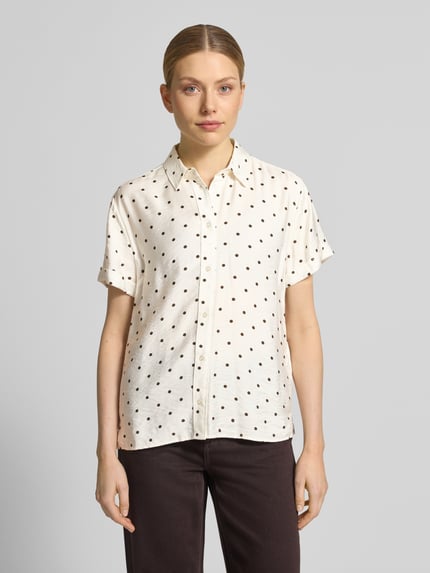 Frauenmodel trägt Regular Fit Bluse aus Viskose-Mix im Allover-Look von Jake*s Casual mit schwarzen Punkten auf cremefarbenem Stoff, Hemdblusenkragen und kurzen Ärmeln mit Aufschlag, Ganzkörperansicht von vorne.
