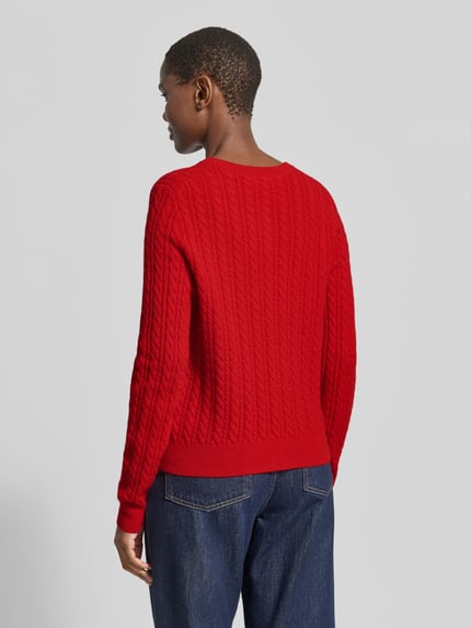 Frauenmodel trägt Regular Fit Strickjacke aus reinem Kaschmir mit Zopfmuster von Christian Berg Woman in Rot, Strukturstrick, Jeans, Ganzkörperansicht Rückansicht.