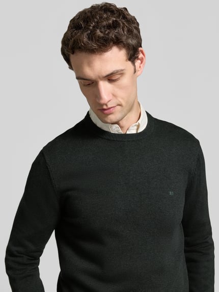 Mannenmodel draagt Regular Fit Strickpullover aus Baumwoll-Woll-Mix van Christian Berg Men, donkergroen, structuur breisel, ronde hals, labelstiksel, katoen-wolmix, borststuk zichtbaar, halve close-up vooraanzicht.