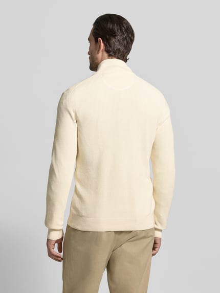 Männermodel trägt Cardigan mit Zweiwege-Reißverschluss und Label-Stitching von Gant aus reiner Baumwolle in Creme, Slim Fit, Stehkragen, Rückenlänge 70 cm, Ärmellänge 64 cm, strukturierte Oberfläche, Ganzkörperansicht Rückansicht.
