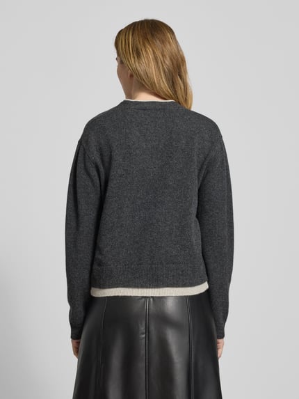 Frauenmodel trägt Cardigan aus Wolle mit V-Ausschnitt Modell 'Tracy' von My Essential Wardrobe, Regular-Fit, Rückansicht, Rückenlänge 55 cm, Ärmellänge 57 cm, feine Stricktextur, dunkles Grau auf glattem Lederrock. Ganzkörperansicht Rückansicht.