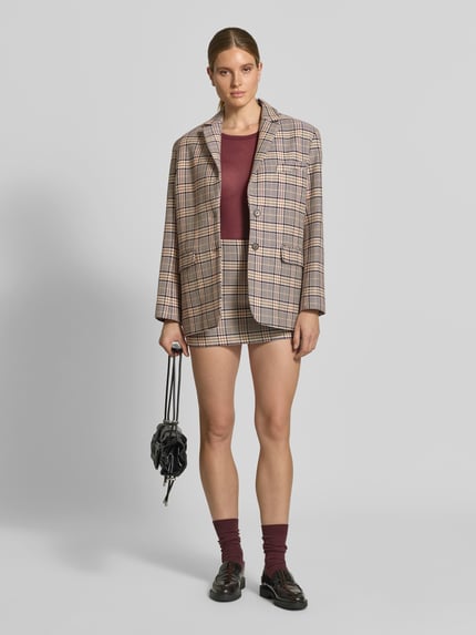 Frauenmodel trägt Minirock aus Viskose-Baumwoll-Mix von Anine Bing mit köpernaher Passform, Nahtreißverschluss, glattem Unterrock und Minilänge, dazu gemusterter Blazer und rote Socken, Ganzkörperansicht von vorne.