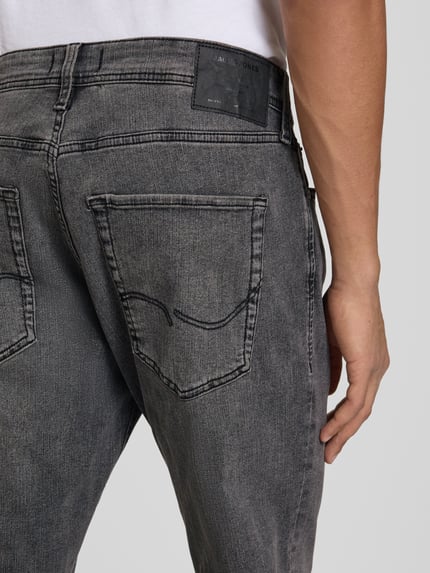 Mężczyznamodel nosi Slim Fit Jeans mit Lyocell-Anteil Model 'Clark' od JACK & JONES, mieszanka bawełny i lyocellu, 5 kieszeni, zapięcie na guzik i zamek błyskawiczny, szara tekstura, detal tylnej kieszeni, Długość wewnętrzna nogawki w rozmiarze 32/32: 78 cm, Szerokość w rozmiarze 32/32: 34 cm, zbliżenie tylnej części.