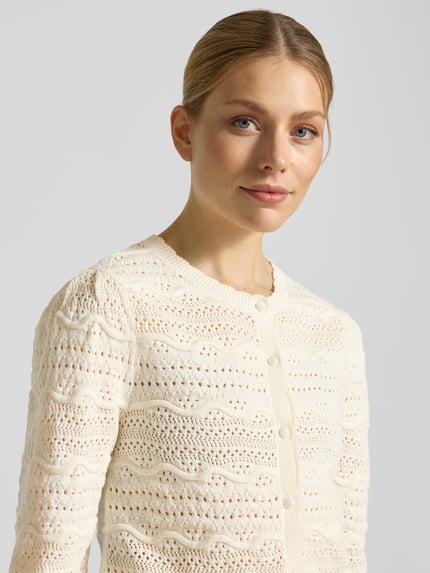 Frauenmodel trägt Strickjacke mit Rundhalsausschnitt Modell 'GANACH' von SUNCOO PARIS in creme, Reine Baumwolle, Regular-Fit, Knopfleiste, Nahaufnahme Oberkörper.