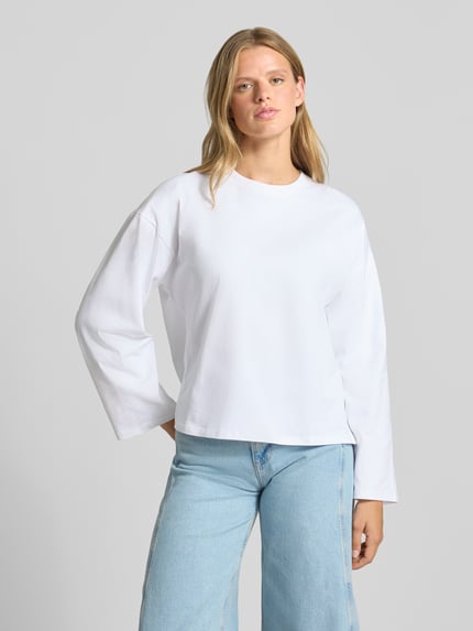 Frauenmodel trägt Oversized Langarmshirt aus reiner Baumwolle von REVIEW in Weiß mit Rundhalsausschnitt, lockerer Passform, Ganzkörperansicht von vorne. Damen Langarmshirt, überschnittene Schultern, Rückenlänge bei Größe S 58 cm.