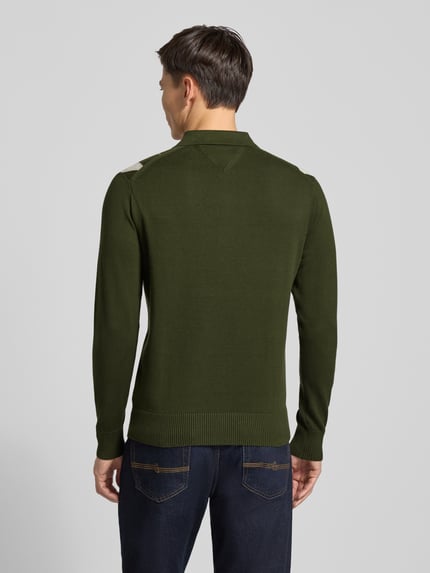 Mannenmodel draagt Regular Fit Strickpullover aus reiner Baumwolle van Tommy Hilfiger in effen donkergroen, rasterruit motief, polokraag, lange mouwen, geribde rompzoom en mouwboorden, gebreide structuur van puur katoen, labelstitching applicatie, ganzkörperansicht rückansicht.