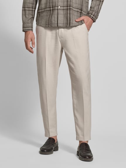 Männermodel trägt spodnie model 'PILOU' von Casual Friday, mieszanka materiałów z lnem, krój regular fit, elastyczny pas, szerokość w rozmiarze M 42 cm, długość wewnętrzna nogawki 73 cm, jasny beż, gładka faktura, Ganzkörperansicht von vorne.