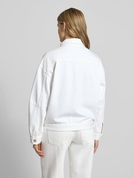Vrouwenmodel draagt jeansjack met borstzakken van Gina Tricot, puur katoen, loose fit, platte kraag, knoopsluiting, ruglengte maat S 63 cm, schouderbreedte 59 cm, borstwijdte 60 cm, mouwlengte 57 cm, geheel wit, rugaanzicht