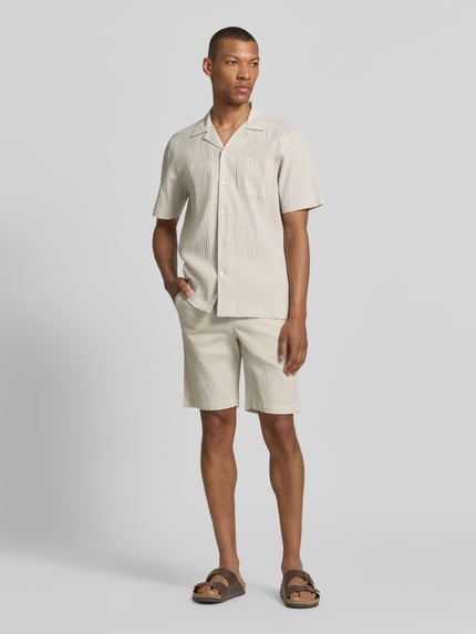 Männermodel trägt Shorts mit elastischem Bund und Strukturmuster von Lindbergh, aus Baumwoll-Mix mit Stretch-Anteil, Loose-Fit, seitliche Eingrifftaschen, in Beige mit dezenter Struktur, Bundweite 42 cm, Innenbeinlänge 25 cm, Ganzkörperansicht von vorne.