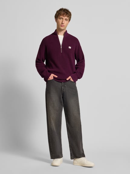 Männermodel trägt Loose Fit Troyer mit gerippten Abschlüssen von Calvin Klein Jeans in Dunkellila, Troyer-Kragen, Label-Detail, Ganzkörperansicht von vorne.