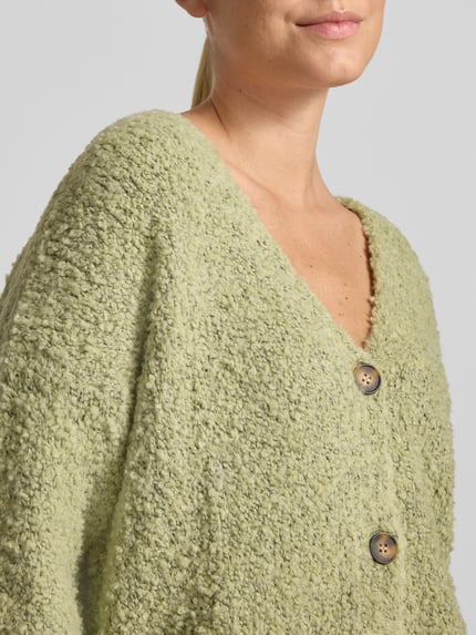 Frauenmodel trägt Cardigan mit V-Ausschnitt Modell 'So44fia' von ZABAIONE, grün, grobe Textur, Knopfleiste, Nahaufnahme Oberkörper. Material-Mix mit Viskose-Anteil, gerader Schnitt.