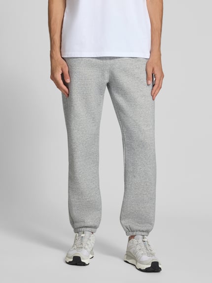 Männermodel trägt Sweatpants mit Label-Detail von Champion in Hellgrau, gerader Schnitt, Baumwollmischung, Ganzkörperansicht von vorne.