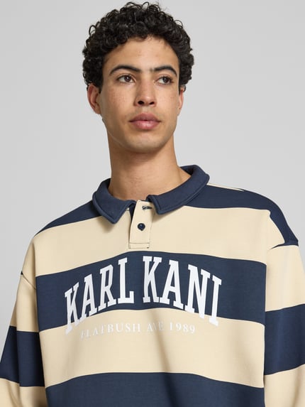 Männermodel trägt Oversized Sweatshirt mit Polokragen Modell 'Heritage' von KARL KANI im Baumwoll-Mix, Logo-Print, Nahaufnahme Oberkörper.