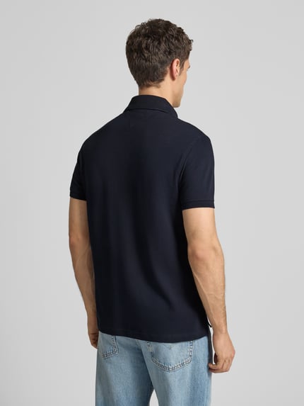 Männermodel trägt Regular Fit Poloshirt mit Logo-Stitching von Tommy Hilfiger aus Baumwoll-Elasthan-Mix in Dunkelblau, Ganzkörperansicht Rückansicht.