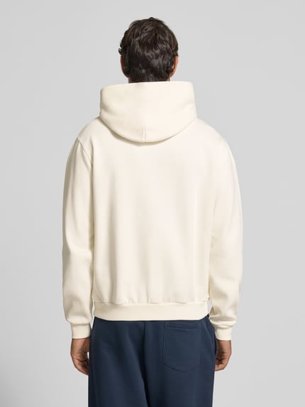 Männermodel trägt Hoodie mit Label-Print von Napapijri in Cremeton mit lockerer Passform, Ganzkörperansicht Rückansicht. Baumwollmischung, Kapuze mit Knopf, Känguru-Tasche, elastische Rippbündchen, Rückenlänge bei Größe M 64 cm, Ärmellänge 73 cm.