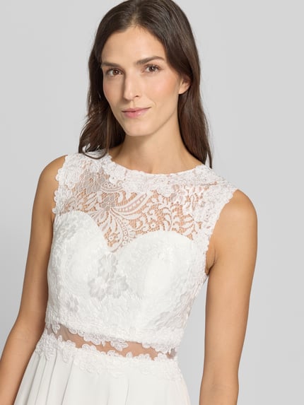 Frauenmodel trägt Cocktailkleid mit Spitze und Rundhalsausschnitt von Mascara, weißer Chiffon, A-Linie, Nahaufnahme Oberkörper.