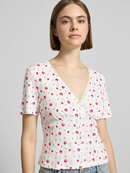 Frauenmodel trägt Blusenshirt in Pointelle-Optik Modell 'Vianne' von OH APRIL aus Reine Baumwolle, Weiß mit rotem Muster, Nahaufnahme Oberkörper.