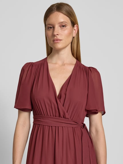 Frauenmodel trägt Abendkleid mit V-Ausschnitt und Bindegürtel von Christian Berg Cocktail in Chiffon, Stufen-Look, Nahaufnahme Oberkörper. Rückenlänge bei Größe 36: 151 cm, Brustweite bei Größe 36: 41 cm, Ärmellänge bei Größe 36: 30 cm.