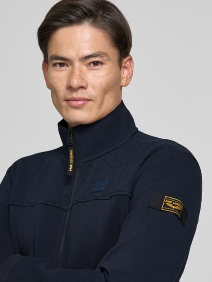 Männermodel trägt Sweatjacke mit Stehkragen und Label-Patch von PME Legend in Dunkelblau, Strukturmuster, Nahaufnahme Oberkörper.