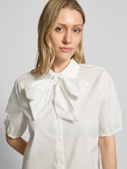 Vrouwenmodel draagt Schluppenbluse mit verdeckter Knopfleiste Modell 'malay' van FREE/QUENT, witte katoenen straight fit blouse met strik en elastische mouwuiteinden, hemdkraag, detailopname bovenlichaam.