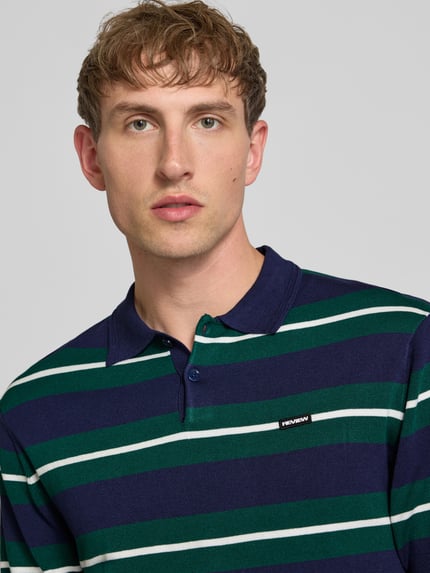 Männermodel trägt Slim Fit Poloshirt aus Viskose-Mix von REVIEW, gestreift in Blau und Grün, Logo-Patch, Nahaufnahme Oberkörper.