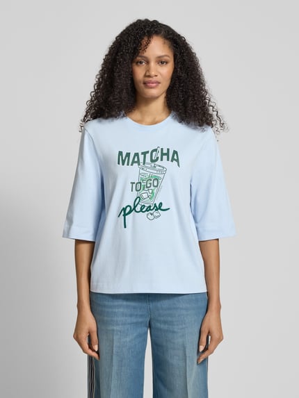 Frauenmodel trägt Slim Fit T-Shirt mit Motiv-Print von Marc Cain in Hellblau, reine Baumwolle, Halbarm, Rundhalsausschnitt, Ganzkörperansicht von vorne.