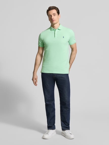 Männermodel trägt 'Slim Fit Poloshirt aus Baumwoll-Mix' von Polo Ralph Lauren in effen groen met logodetail en polokraag, piqué katoenmix, slim fit pasvorm, korte mouwen, geribde mouwboord, asymmetrische rompzoom met zijsplitten. Ganzkörperansicht von vorne.