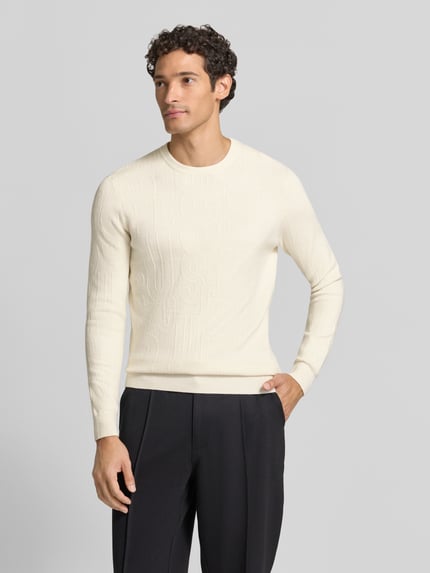 Männermodel trägt Strickpullover aus Viskose-Mix Modell 'NESTOR' von GUESS in Offwhite, Slim Fit, Allover-Look, Ganzkörperansicht von vorne.