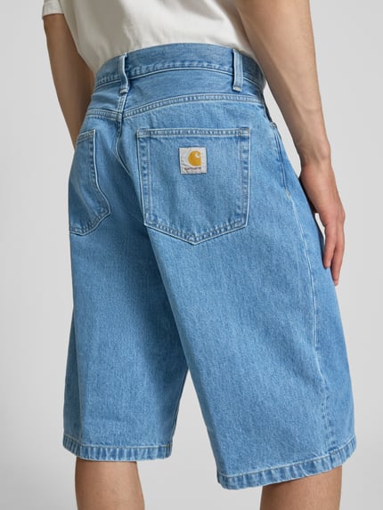 Männermodel trägt Jeansshorts mit Eingrifftaschen Modell 'Langdon' von Carhartt Work In Progress, hellblau, reine Baumwolle, Ganzkörperansicht Rückansicht.