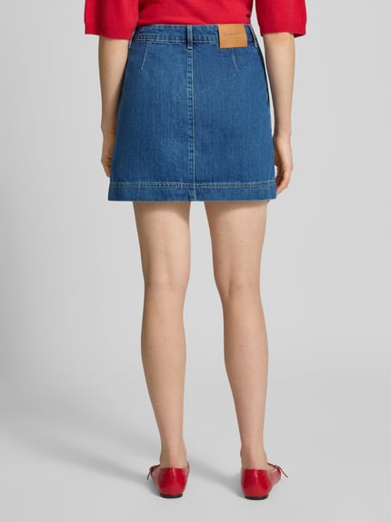 Kobiece modelka nosi Jeansrock aus Baumwolle mit Knöpfen von Gant, spódnica jeansowa z bawełny, prosty krój, spódnica mini, szerokość w rozmiarze 36: 37 cm, całkowita długość w rozmiarze 36: 41 cm, widok całej sylwetki od tyłu.