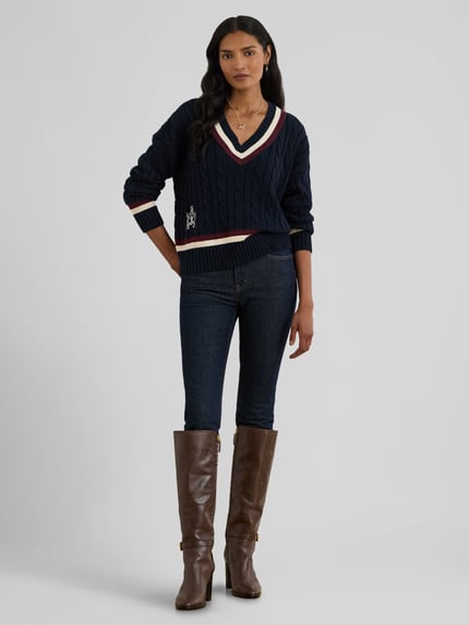 Frauenmodel trägt Regular Fit Strickpullover aus reiner Baumwolle von Lauren Ralph Lauren in Optik: Unifarben mit Zopfmuster, Logo-Detail, Label Stitching und Kontraststreifen, gerippte Abschlüsse, V-Ausschnitt, Langarm, Materialverarbeitung: Strick, Ganzkörperansicht von vorne.